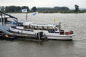 Rondvaartboot aangemeerd aan een steiger op de Rijn met twee wapperende RW-vlaggen en passagiers aan boord